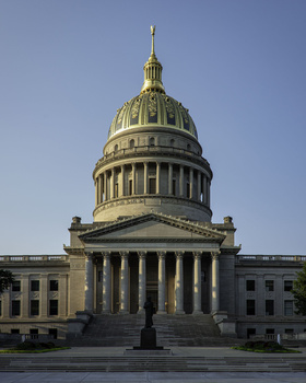Neoclassical government building with golden dome and columned portico against clear blue sky.