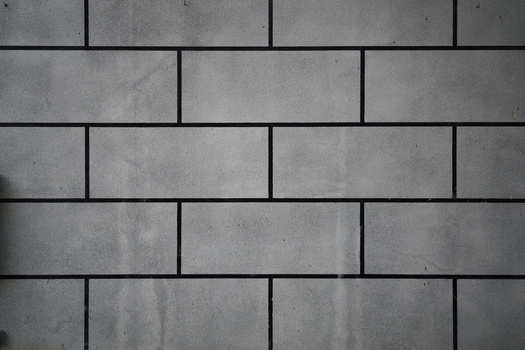 Stacked concrete brick wall with running bond pattern and dark mortar joints.