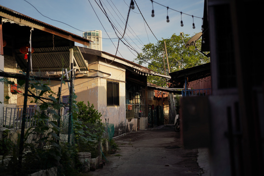 Narrow alley between weathered buildings with overhead power lines and dappled morning light.