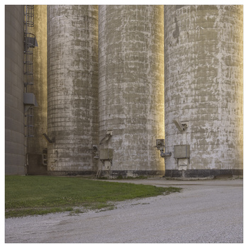 Tall cylindrical concrete structures with vertical ribbing and golden accent strips, photographed from ground level against green lawn.