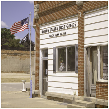 Small-town brick post office building with white trim and American flag flying outside.