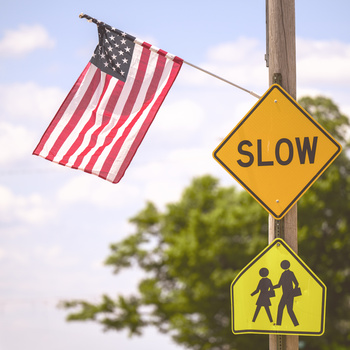 American flag and yellow traffic signs mounted on a wooden pole against a cloudy sky.