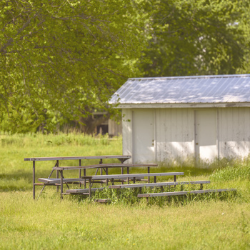 Weathered wooden picnic table and bench seating on grass near a white shed with metal roof.