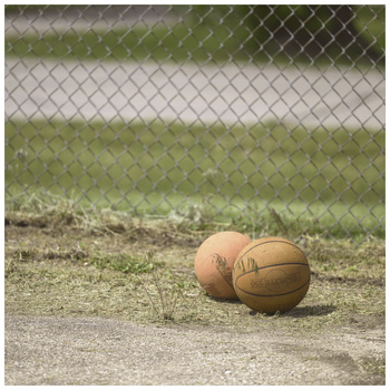 Two worn basketballs resting on concrete ground against a chain-link fence.