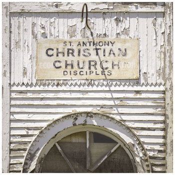 Weathered wooden church sign reading "St. Anthony Christian Church Disciples" with peeling white paint and an arched window below.