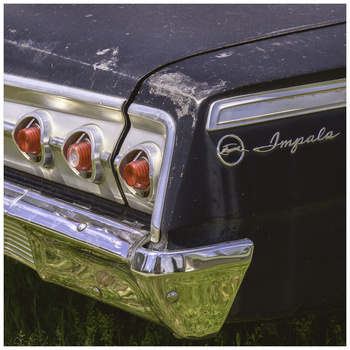 Close-up of a classic car's rear quarter panel showing triple taillights and chrome trim details.