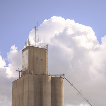 Concrete grain elevator tower with antenna array against puffy white cumulus clouds.