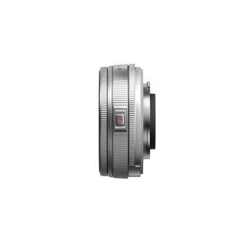Silver mirrorless camera lens with electronic contacts and manual focus ring, shown in profile view.