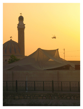 Silhouetted mosque with minaret and dome against golden sunset sky with tent canopy in foreground.