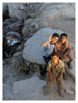 Three children standing on rocky ground, looking up toward the camera from below.