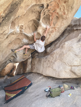 Rock climber scaling a steep sandstone face using climbing holds and technique.