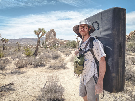 Hiker with large backpack standing beside Joshua tree in desert landscape.