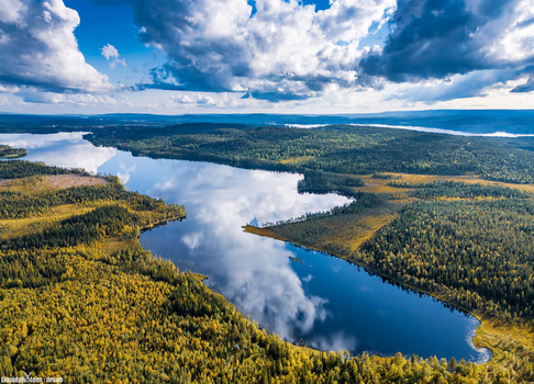 Aerial view of interconnected lakes surrounded by dense boreal forest under a dramatic cloudy sky.