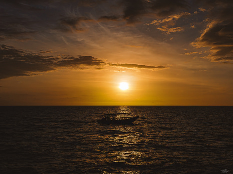 Golden sunset over calm ocean with silhouetted boat on the horizon.