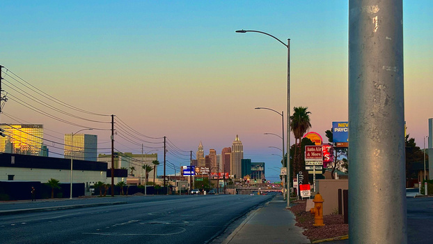 Desert city skyline at dusk with illuminated casino buildings and street-level perspective from sidewalk.