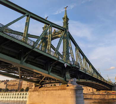 Historic steel bridge with green girders and yellow diagonal bracing spanning a river, photographed in golden hour light.