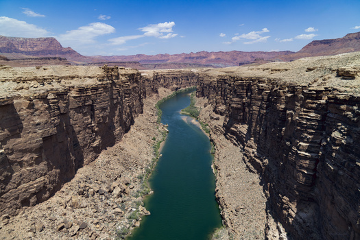 Turquoise river winding through layered rock canyon in vast desert landscape.