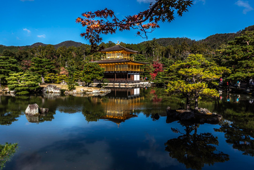 Golden pavilion reflected in still water surrounded by autumn foliage and forested mountains.
