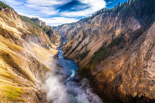 Deep canyon with steep forested walls and a river flowing through mist below.