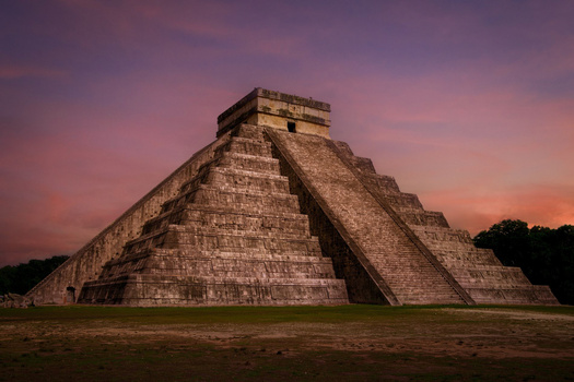 Ancient stone pyramid with stepped sides and flat top platform photographed against a dramatic purple and orange sunset sky.