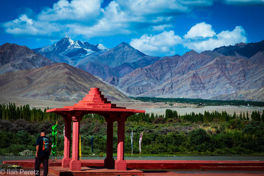 Red pavilion structure framing snow-capped mountain peaks and valley landscape.