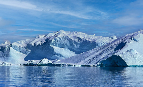 Snow-covered mountain peaks rising above calm blue water with small icebergs.