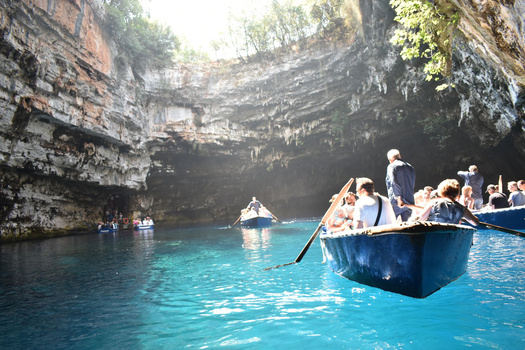 Blue rowboat filled with tourists navigating turquoise water inside a massive limestone cavern with towering rock walls.