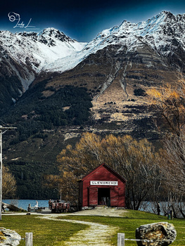 Red barn nestled in an alpine valley beneath snow-capped mountain peaks.