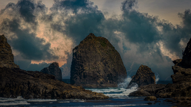 Dramatic rocky sea stacks rising from turbulent ocean waters beneath moody, cloud-filled sky.