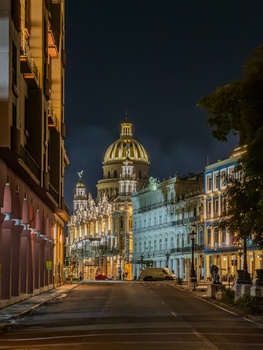 Illuminated classical dome and historic buildings along a European street at dusk.