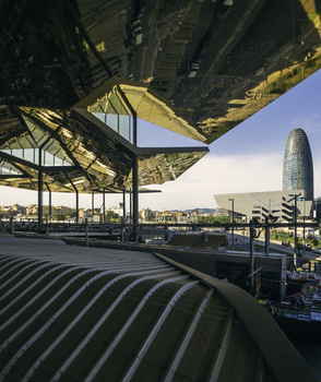 Architectural photograph taken from under a modern building overhang, looking up at geometric steel structures and clear sky.