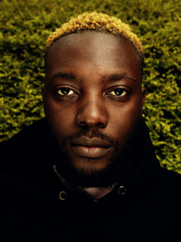 Portrait of a person with golden hair against a moss-textured green backdrop.