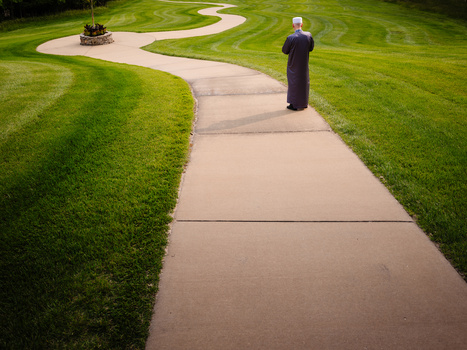 Person standing on a concrete pathway between manicured green lawns with curved landscaping features.