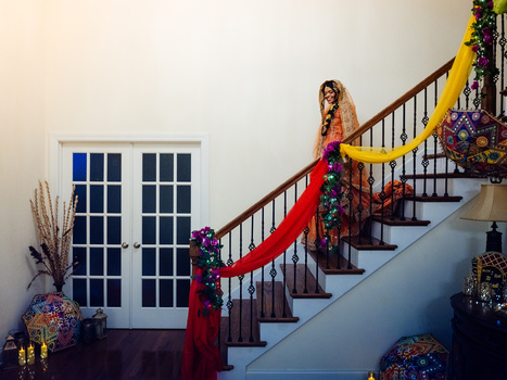 Woman in colorful traditional dress poses on a staircase with red carpet and yellow garland railing.