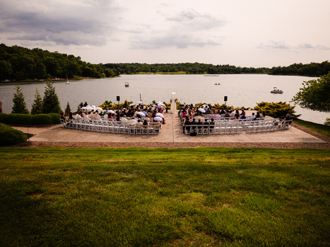 Aerial view of two waterfront pavilions filled with people on a sandy beach beside a calm river.