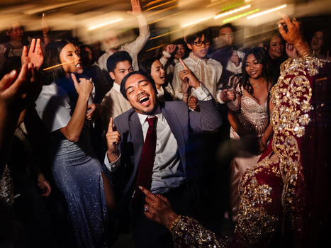 Diverse group of people dancing and celebrating at an indoor event with warm overhead lighting.