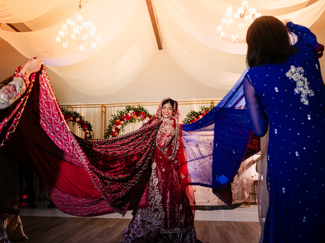 Woman in embellished red lehenga posing under draped tent with decorative fabrics and hanging lights.