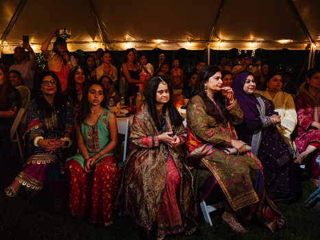 Women in vibrant traditional South Asian clothing seated under a tent with warm overhead lighting.