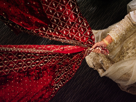Ornate red beaded bridal lehenga detail showing intricate embroidery and embellishments on silk fabric.