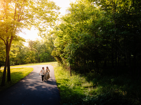 Two figures walking on a tree-lined path with golden sunlight filtering through the canopy.
