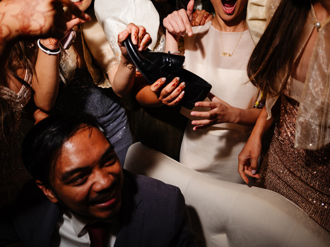 Group of people gathered around a black clutch purse at what appears to be a social event, with warm indoor lighting.