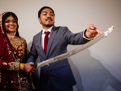 Couple in formal attire holding a curved sword, posed against a neutral background.