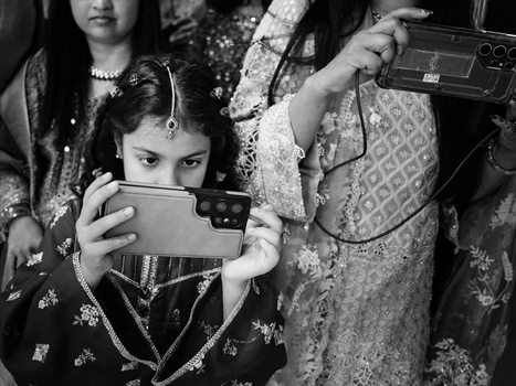 Child holding vintage handheld camera while adults with cameras stand nearby in black and white photograph.