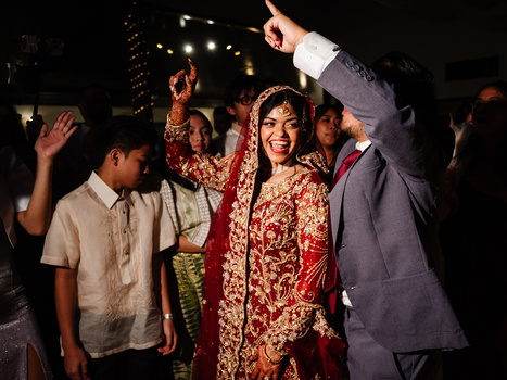 Bride in red ornate wedding attire celebrating with guests under warm evening lighting.