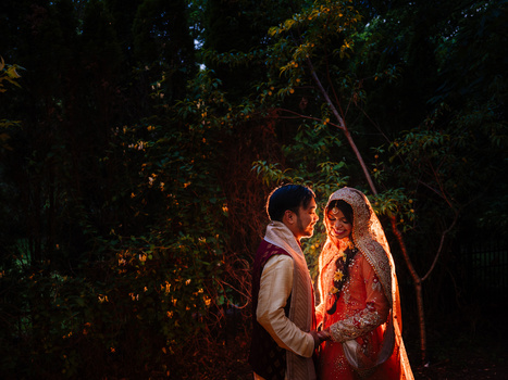 Couple in traditional wedding attire embraced among trees in warm golden light.