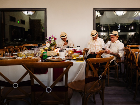 Four people in straw hats seated at a dining table with place settings and floral centerpiece.