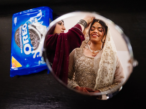 Two women smiling while holding a blue Oreos package, photographed through a circular lens with selective focus.