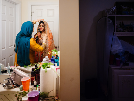 Two people wearing colorful traditional clothing embrace in a bathroom doorway surrounded by cosmetics and personal care items.