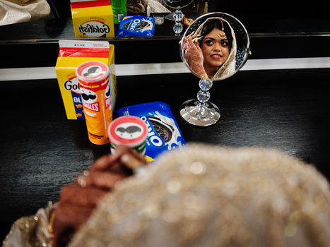 Decorative mirror with woman's reflection surrounded by colorful bottles and packages on black surface.