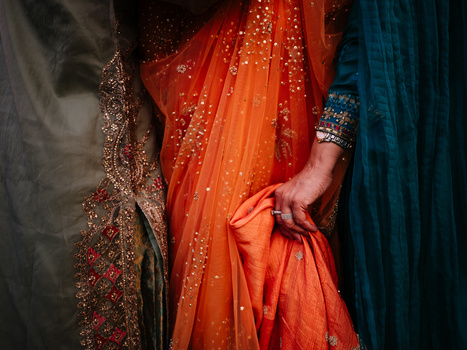 Close-up of ornate fabrics with embellished red and orange draping held in hand against darker colored garments.